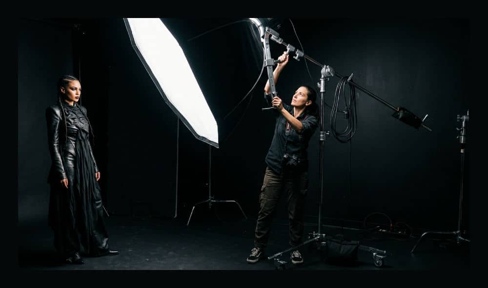 A professional photographer adjusts a strobe light modifier in a blackout studio environment.