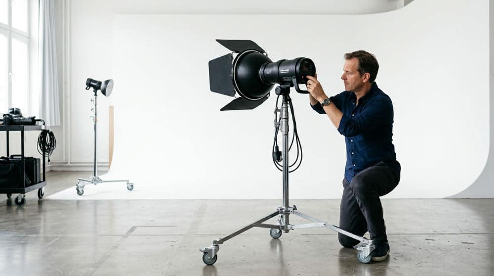 A photographer setting up strobe lighting for a commercial shoot on a professional photography cyclorama wall.
