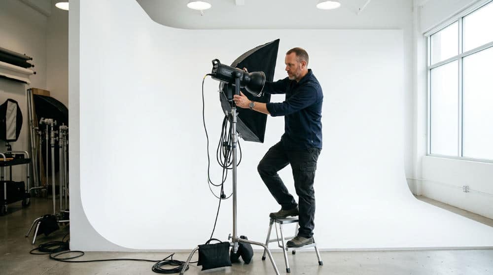 A photographer setting up lighting for a session in a professional cyclorama wall studio.