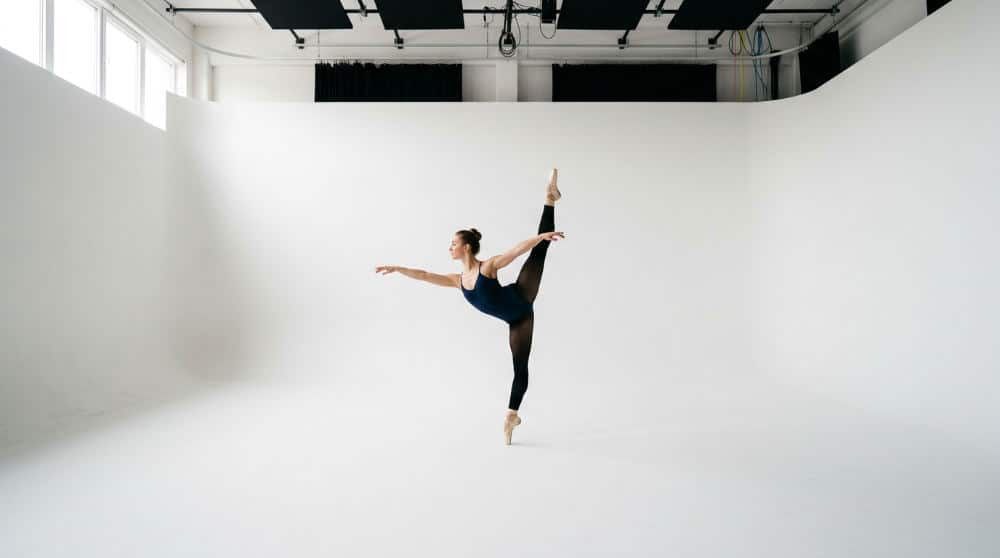 A dancer performing a technical movement on a white cyclorama wall at Lightz Out Studios in San Diego.