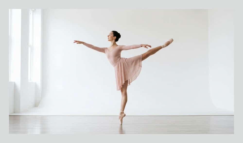 A dancer demonstrating a technical first arabesque pose against a white cyclorama wall for an audition portfolio.