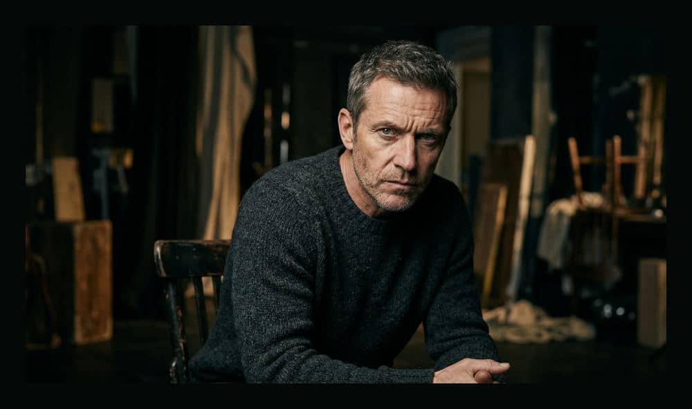 A dramatic theatrical headshot of a male actor with focused eyes and moody studio lighting.
