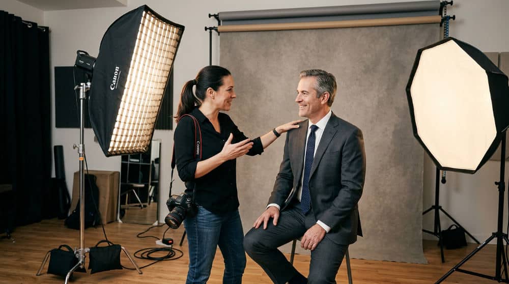 A male photographer coaching a client for professional headshots at a San Diego studio with softbox lighting and a gray backdrop.