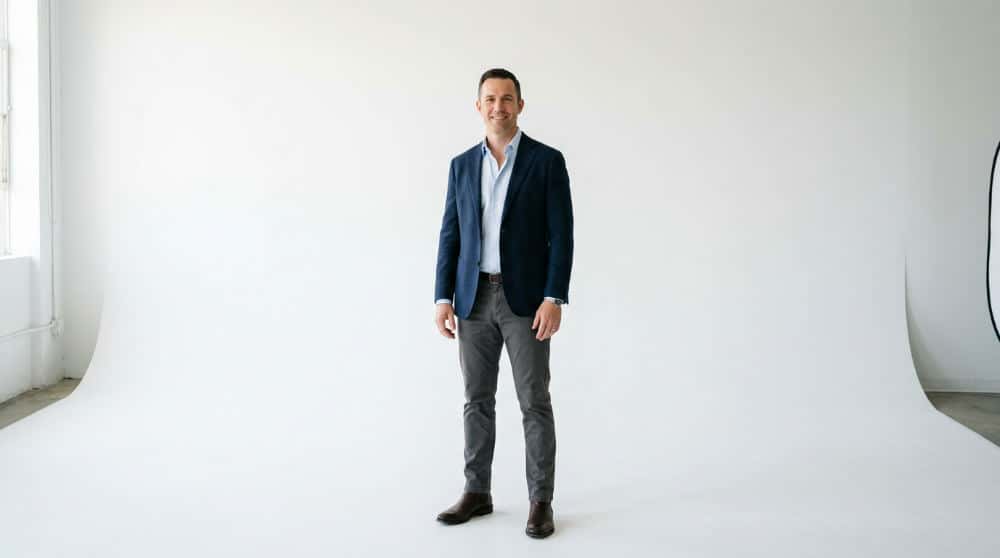 A professional man in a grey blazer standing in front of a white cyclorama wall in a San Diego studio.