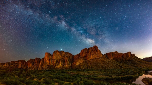 Desert rock formations silhouetted against a starry night sky with the Milky Way visible overhead.