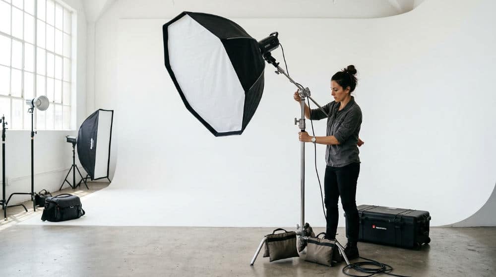 A photographer using professional strobes and modifiers to light a model against a white photography cyclorama wall.
