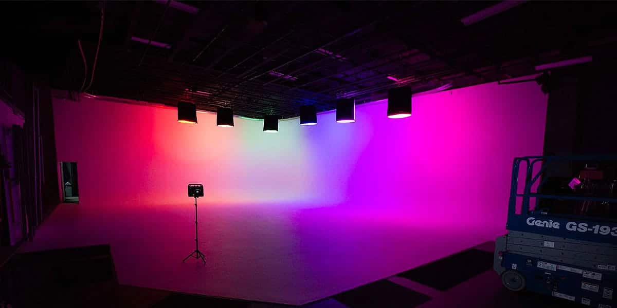 Vibrant view of our Stage A at Pixthis Stage Rentals and Productions in Portland, showcasing a cyclorama wall with colorful lighting, a camera on a tripod, and production equipment, ideal for video editing and color grading in Portland.